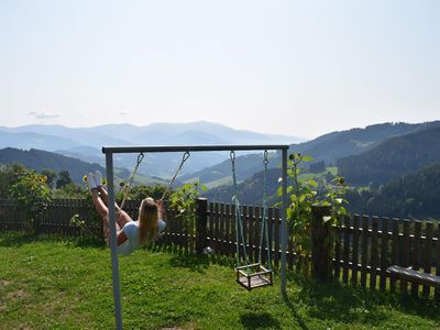 Grünfläche mit Schaukel, Sandkiste und kleiner Feuerstelle und herrlichem Blick auf die Alpenlandschaft