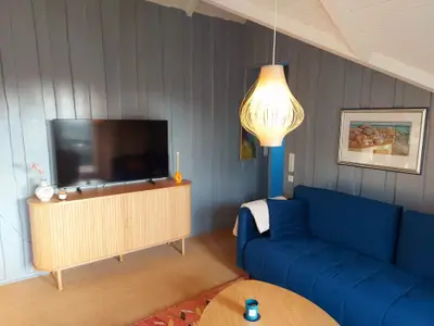 Wohnzimmer mit Couch, TV, Kamin und großen Fenstern