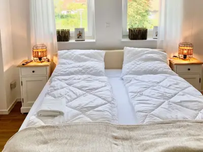 Doppelbett mit weißen Bettdecken und Nachttischen.