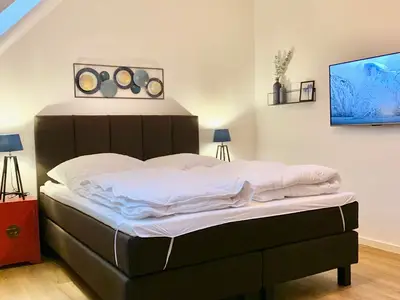 Schlafzimmer mit Doppelbett, Nachttischen und Fernseher.