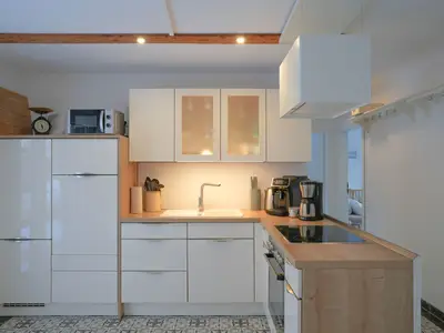 Eine helle, moderne Küche ausgestattet mit weißen Schränken, einem Kochfeld und Elektrogeräten.