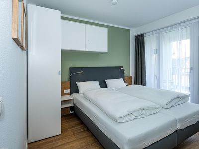 Schlafzimmer mit Doppelbett, Kleiderschrank und Zugang zum Balkon