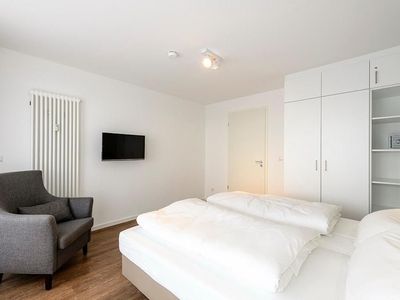 Schlafzimmer mit Doppelbett, Sessel, Kleiderschrank und TV
