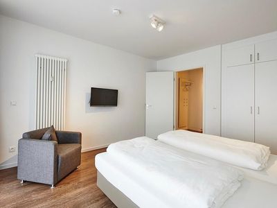 Schlafzimmer mit Doppelbett, Sessel, Kleiderschrank und TV