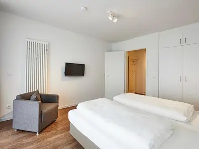Schlafzimmer mit Doppelbett, Sessel, Kleiderschrank und TV