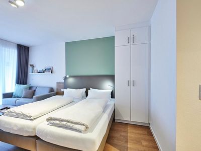 Wohn-Ess-Schlafbereich mit Sofa, Esstisch, Sitzgelegenheit und Doppelbett sowie Zugang zum Balkon