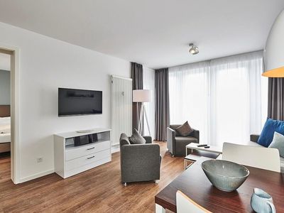 Wohn-Essbereich mit Couch, Flatscreen TV, Esstisch, Sitzgelegenheit und Zugang zum Balkon