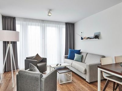 Wohn-Essbereich mit Couch, Sessel, Esstisch und Zugang zum Balkon