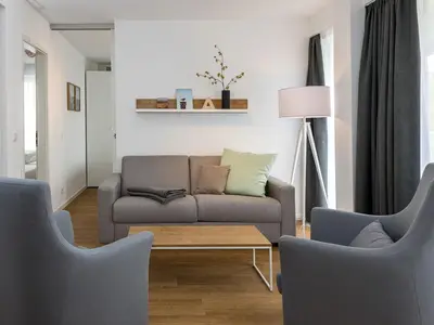 Wohnbereich mit Sofa, Sessel, Couchtisch und Zugang zum Balkon