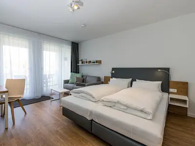 Wohn-Ess-Schlafbereich mit Sofa, Esstisch, Sitzgelegenheit und Doppelbett sowie Zugang zum Balkon