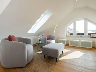 Wohnbereich mit zwei Sesseln, großem Fenster und Sideboard