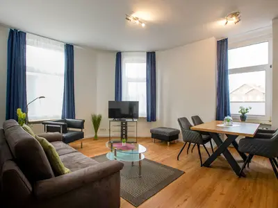 Blick von der Eingangstür zum Wohnbereich, Sofa, Schrankbett und TV sowie Esstisch mit Stühlen