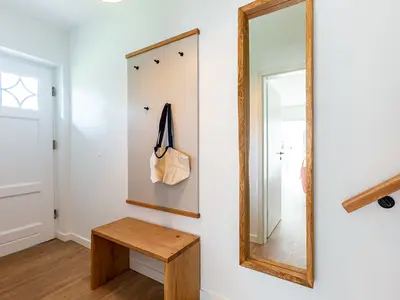 Eingangsbereich mit weißer Tür, Holzbank, Garderobe mit Tasche und großem Wandspiegel.