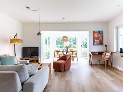 Wohnzimmer mit Sofa, rotem Sessel, TV, Essbereich am Fenster und Schreibtisch.