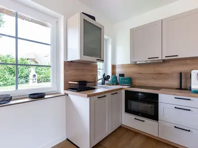 Moderne L-förmige Küche mit hellen Fronten, Holzarbeitsplatte und Fensterblick.