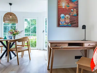 Essbereich mit Holztisch und Stühlen, daneben Schreibtisch mit Bild an der Wand.