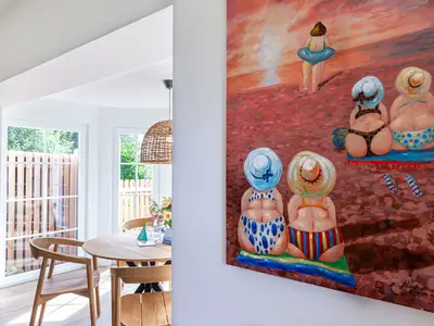 Buntes Strandgemälde an der Wand, daneben Essbereich mit Holztisch und Stühlen.