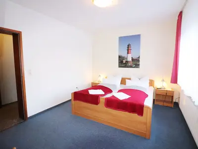 Schlafzimmer mit Doppelbett, bezogenes Bett, Nachttisch mit Tischleuchte, Bild vom Büsumer Leuchtturm