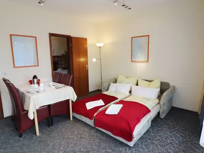 Wohnzimmer mit Schlafcouch, Esstisch und anliegende Küche
