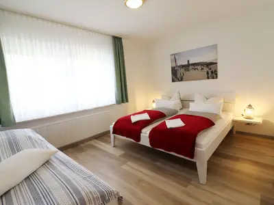 Schlafzimmer mit Doppelbett, extra Bett, Nachttisch mit Tischleuchte, Bild vom Büsumer Leuchtturm