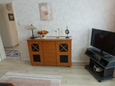 Sat TV und Komode mit Gläser und Spiele zur Unterhaltung. Laminat Fußboden. Im Sitzbereich liegt ein Teppich.