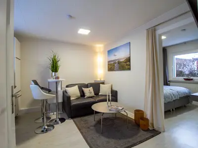 Wohn- und Schlafbereich der Nautic Lounge – Beach House 2 mit gemütlichem Sofa, Essbereich & Boxspringbett – modern.