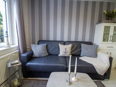 Gemütliches Sofa im maritimen Stil der Nautic Lounge – Beach House 1 mit Blick auf die Fensterfront.