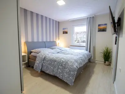 Schlafzimmer der Nautic Lounge – Beach House 1 mit Boxspringbett, Flat-TV und gemütlichem Ambiente.