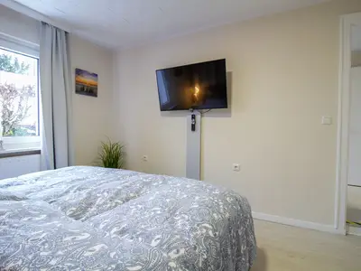 Schlafzimmer der Nautic Lounge – Beach House 1 mit Fenster, Smart-TV und gemütlicher Bettwäsche.