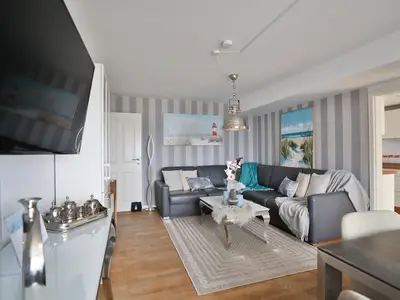 Nautic Lounge – Sea View: Heller Wohnbereich mit Ecksofa, TV und moderner Küche.