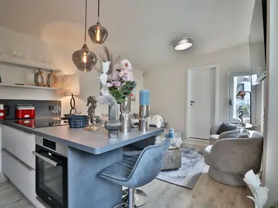 Nautic Lounge – Beach Garden: Offene Küche mit Essbereich und gemütlicher Sitzecke im modernen Ferienapartment Haffkrug.
