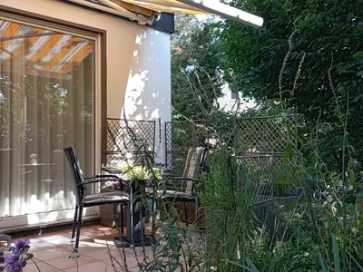 Die Terrasse verfügt über einen Gartentisch mit Stühlen, Markise und einem ausziehbaren Gartensofa