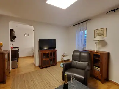 Fernseher und Sessel, im Hintergrund die Küche