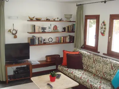 Ansicht Wohnzimmer mit Sofa, TV und Stereoanlage. Alle Fenster sind mit einer Sonnenblende ausgestattet