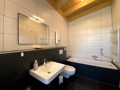 Badezimmer mit WC, Badewanne sowie Waschmaschine und Trockner.