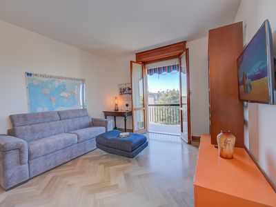 Wohnzimmer mit Schlafsofa, Bücherregal, Smart-TV und Zugang zum Balkon