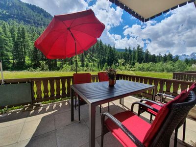 Große Terrasse mit Blick auf die Berge und den Wald. Ausgesattet mit Tisch, Stühlen, Sonnenliegen und Sonnenschirm.