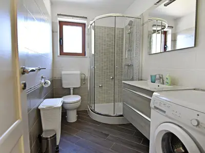 Das Badezimmer mit Dusche, WC, Waschbecken mit Schrank und Spiegel, Waschmaschine