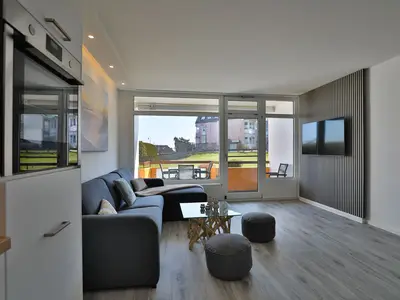 Strandkoje 105 Scharbeutz: Helles Wohnzimmer mit gemütlicher Couch, TV und Balkon mit Teilmeerblick.