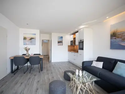 Strandkoje 105 Scharbeutz: Offener Wohnbereich mit moderner Küche, Esstisch und gemütlicher Couch.