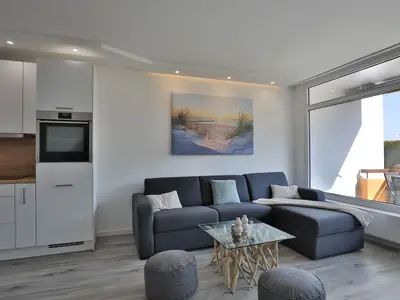 Strandkoje 105 Scharbeutz: Helles Wohnzimmer mit gemütlicher Schlafcouch, modernem Dekor und großem Fenster zum Balkon.