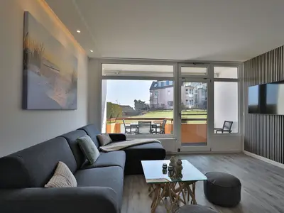 Strandkoje 105 Scharbeutz: Wohnzimmer mit Schlafcouch und Zugang zum sonnigen Balkon mit Teilmeerblick.