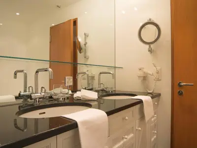 Das elegante, helle Badezimmer verfügt über zwei Waschbecken, Badewanne und Duschkabine