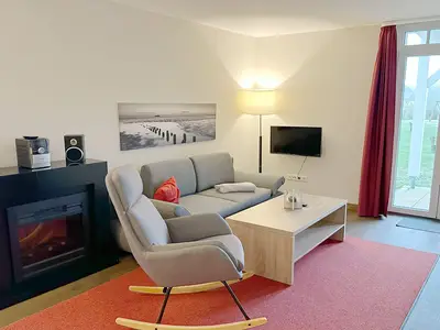 Wohnbereich mit Couch, Schaukelstuhl, Elektrokamin, Flatscreen TV und Zugang zur Terrasse