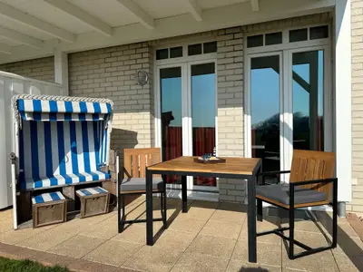 Überdachte Terrasse mit Strandkorb, Sitzgelegenheit und Grünfläche