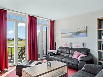 Wohnbereich mit Sofa, Sessel, Couchtisch und Zugang zum Balkon