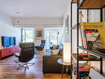 Offener Wohnbereich mit Zugang zur Terrasse, integrierter Küche, Esstisch, ausziehbarer Couch, Relaxsesseln, Smart-TV