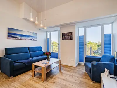 Wohn/Essbereich: Couch und Sessel, TV, Zugang zum Balkon mit Tisch und Stühlen