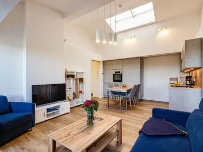 Wohn/Essbereich: Couch und Sessel, TV, Zugang zum Balkon mit Tisch und Stühlen