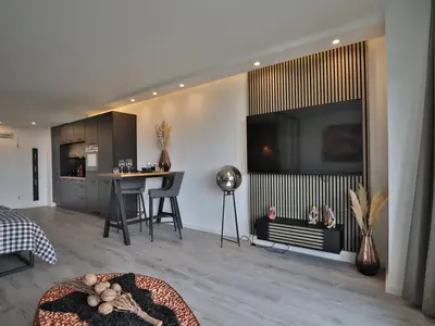 Strandkoje 7: Moderner Wohnbereich mit TV-Wand, Bartisch und viel Licht durch bodentiefe Fenster.